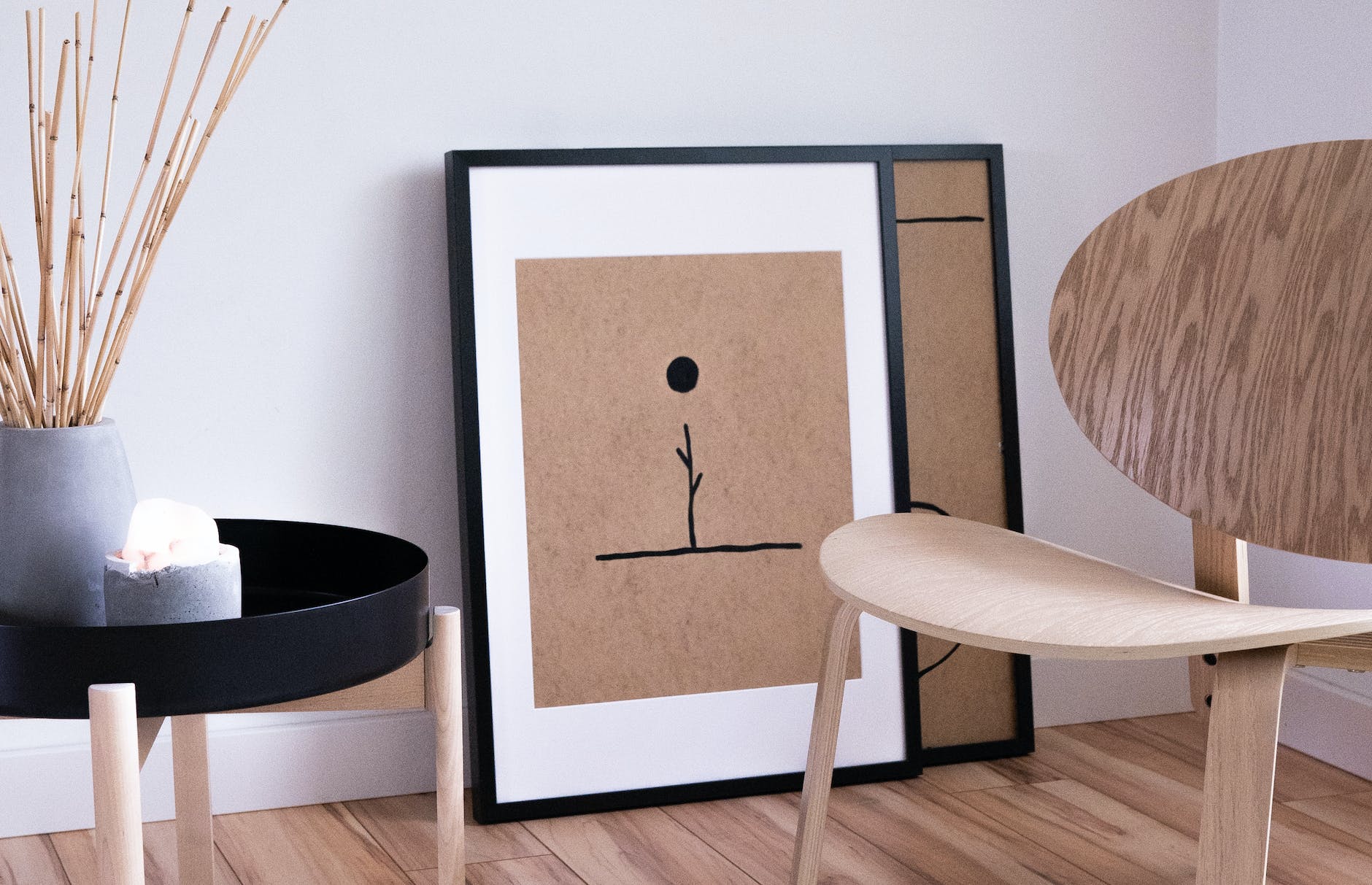Affiche minimaliste encadrée posée au sol près d’un fauteuil en bois